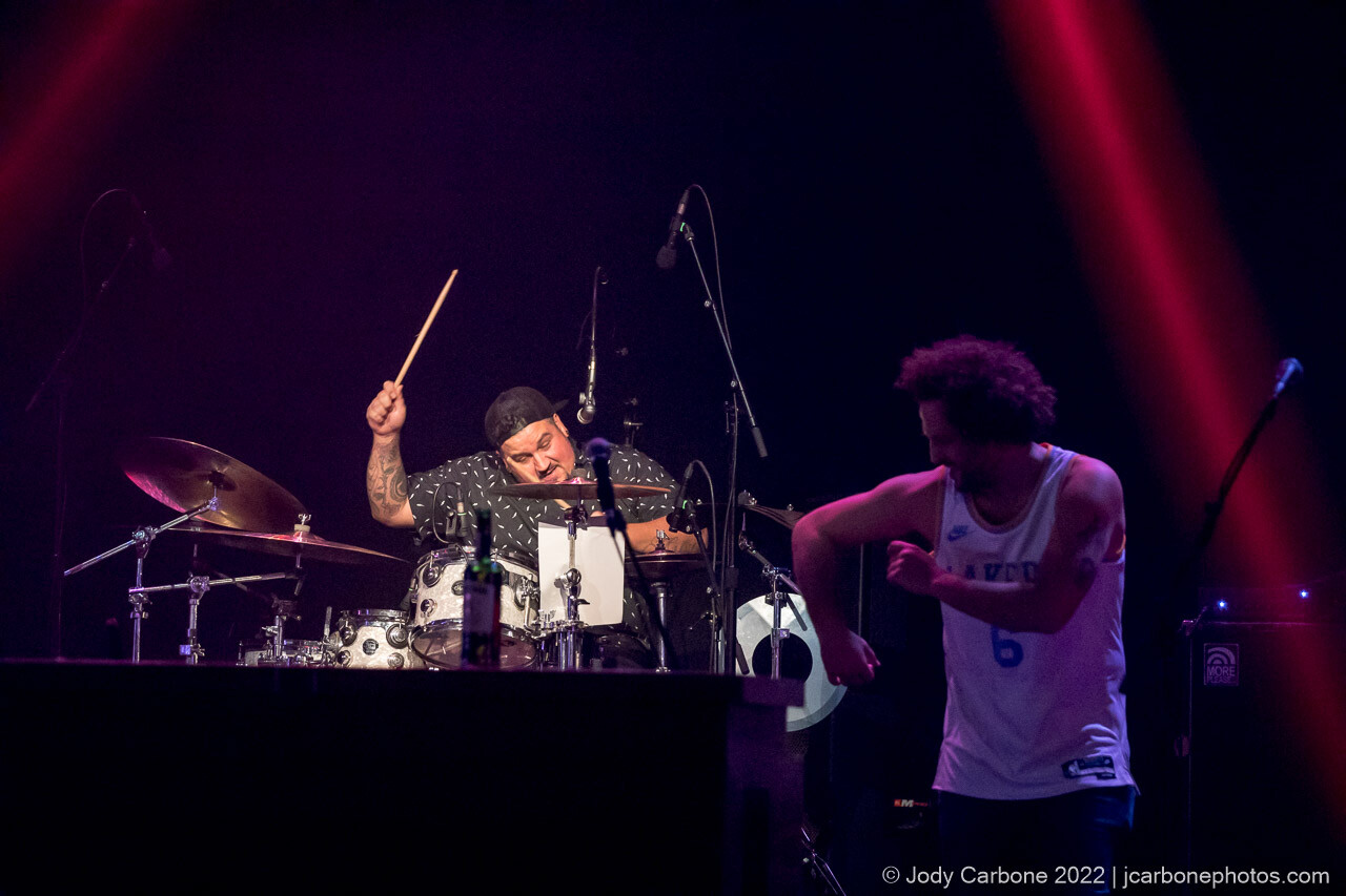 Action concert photography - Andy Frasco dances in foreground while drummer Andee plays under bright light