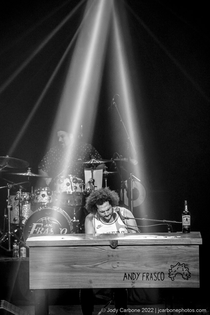 Andy Frasco plays piano under bright white spotlights in this black and white concert photo