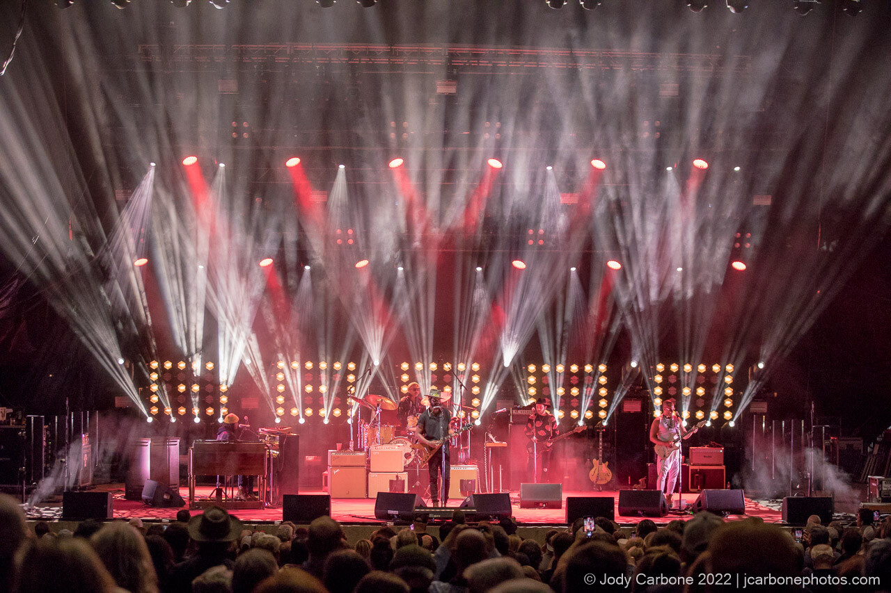 Red background with white beams of light surround Gary Clark Jr. and band