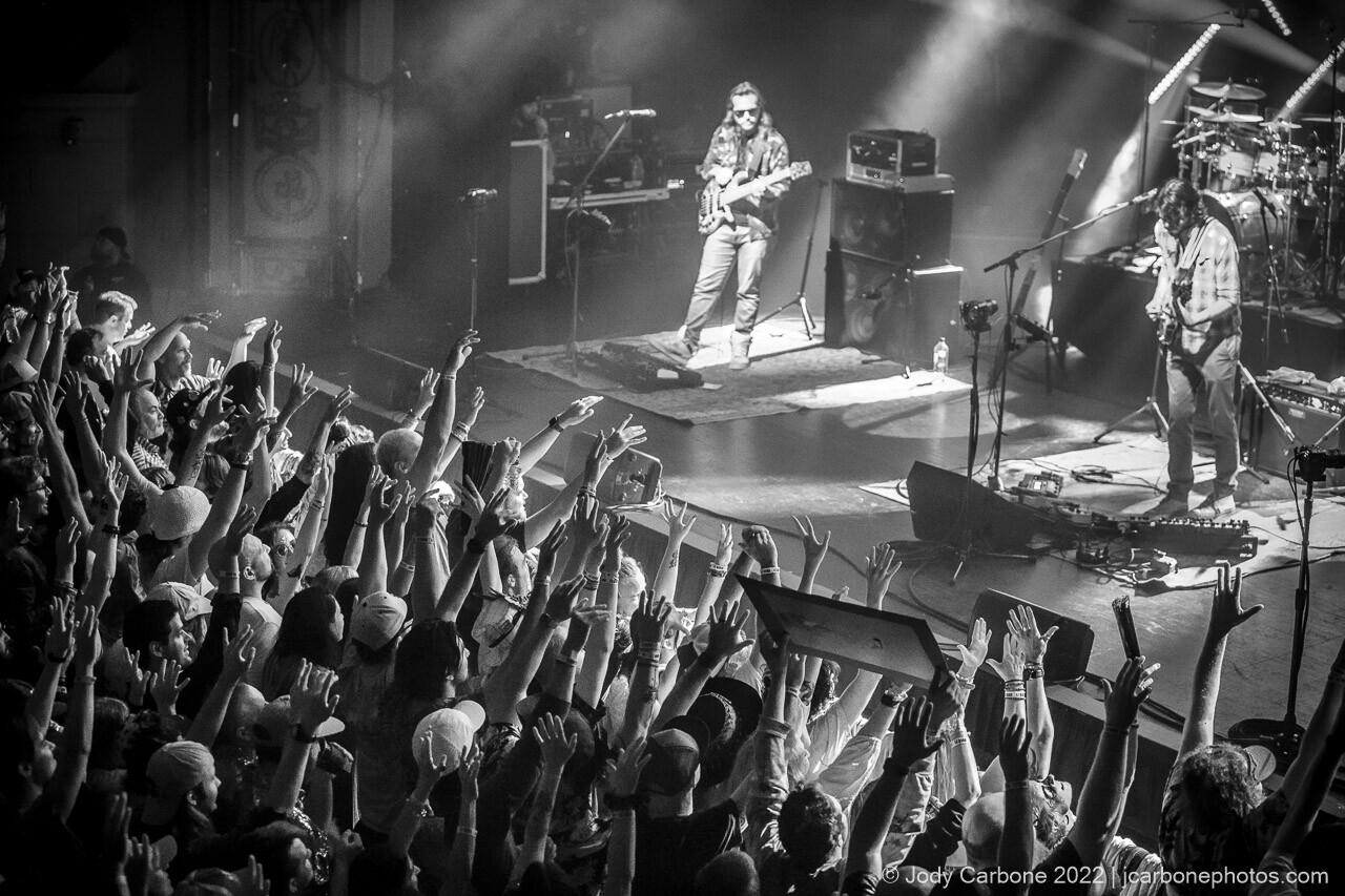 Black and white concert photography - Goose onstage while crowded fans cheer with arms raised